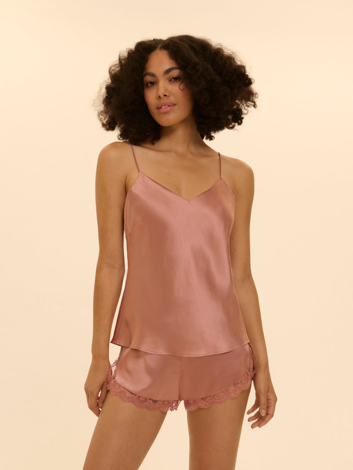 Woman wearing a pink silk tank and shorts pajama set  with lace trim on a beige background