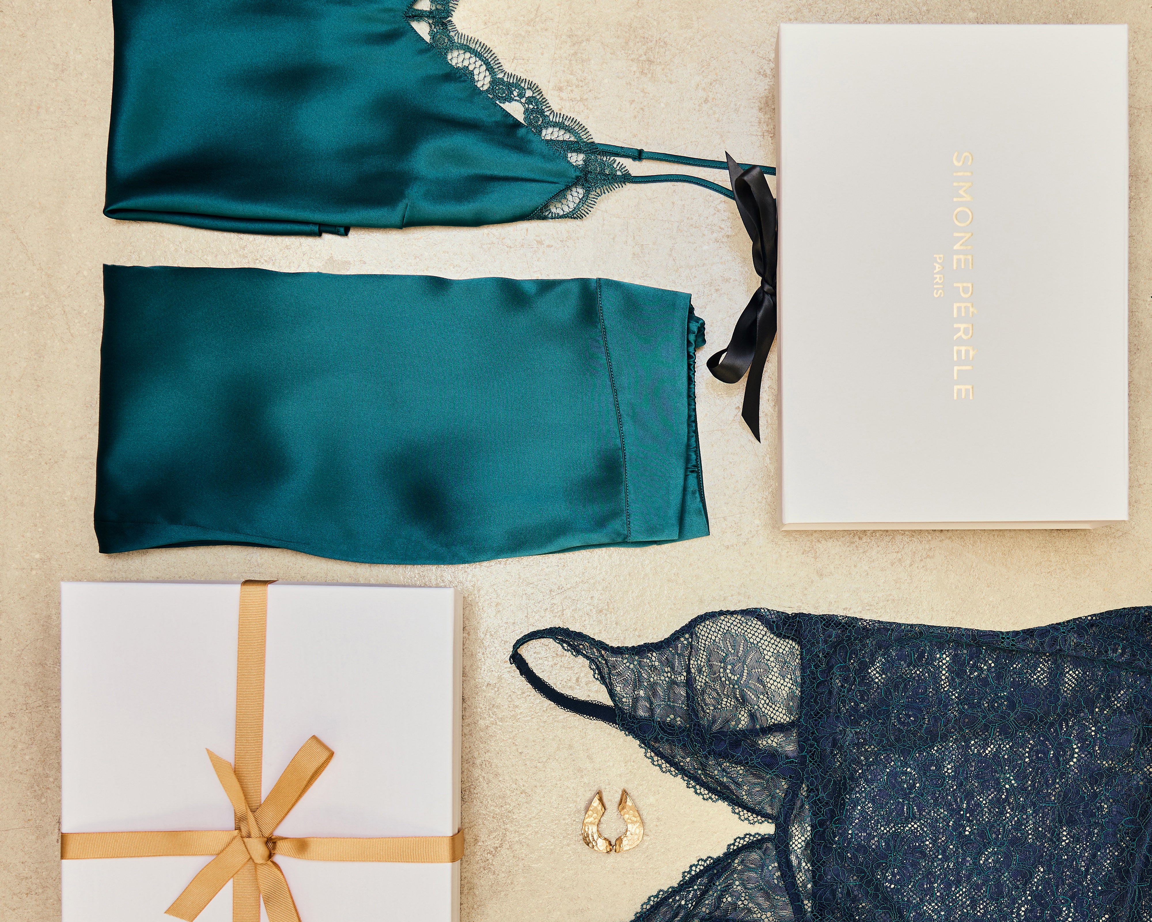 Emerald silk lounge set and bodysuit with a Simone Perele gift box and gold bow on a beige background