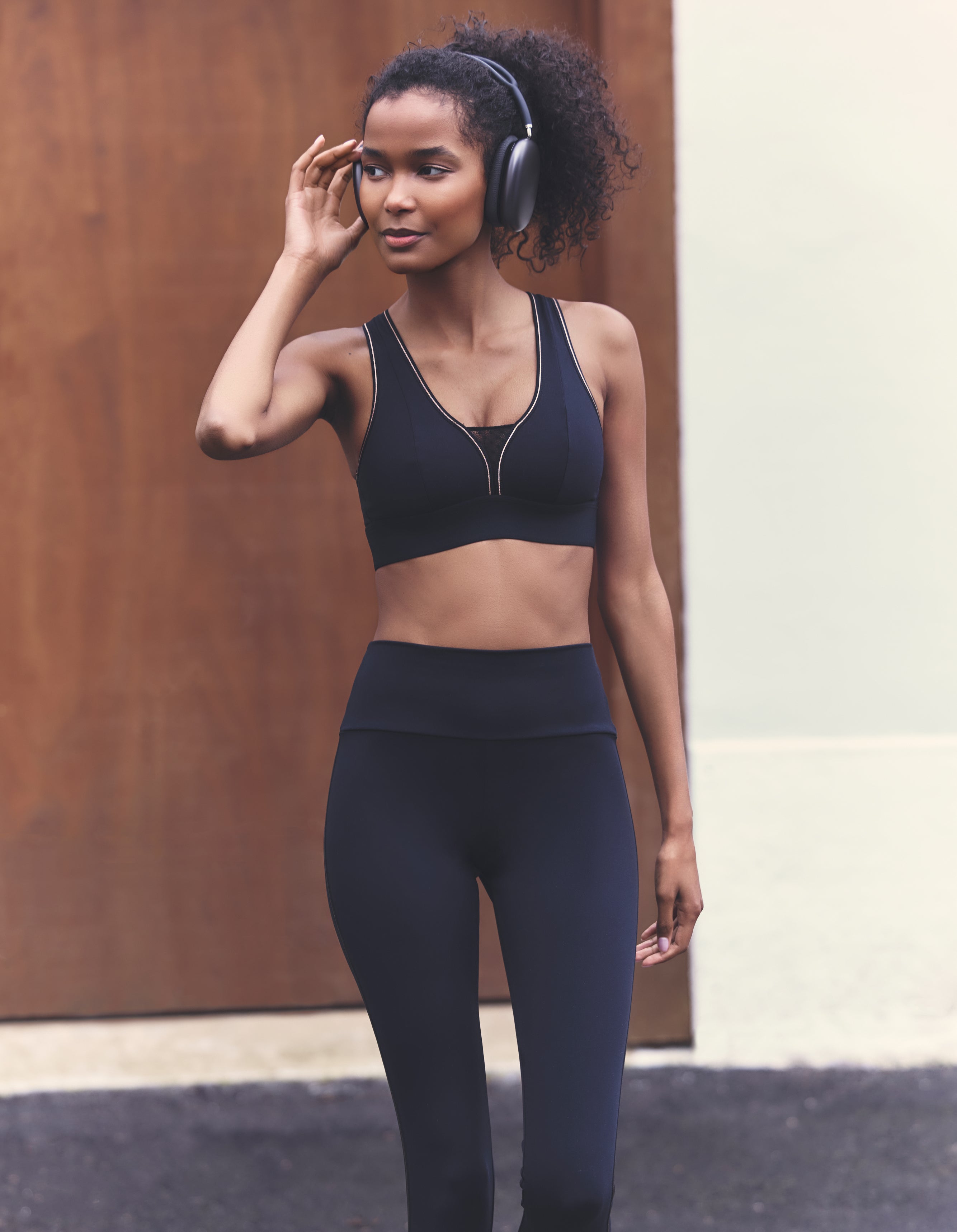 Woman in black athletic wear with headphones, standing outdoors.